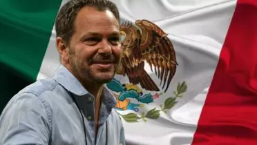 Santiago Baños sonriendo y al fondo la bandera de México / Foto Getty